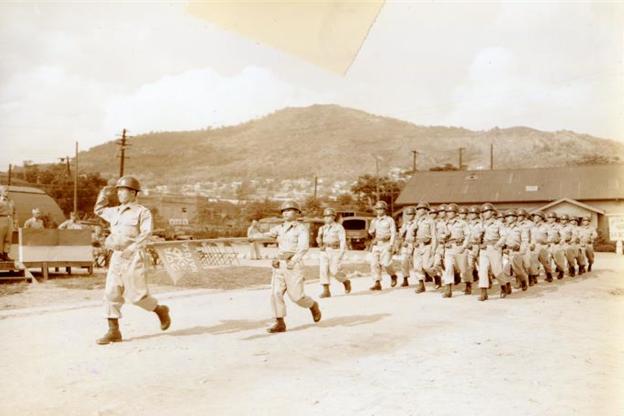 1955年，駐韓美軍附編韓軍（KATUSA）官兵們分列行進之貌（今日的龍山Camp Conier，照片背景為1950年代的首爾南山）